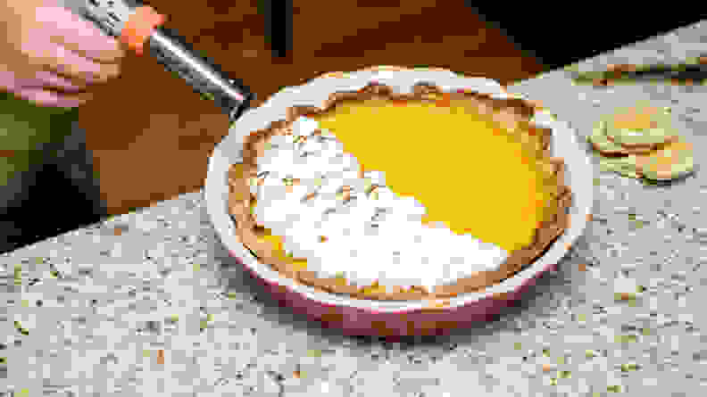 A hand using a butane torch to scorch meringue atop a pumpkin pie.