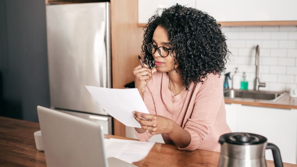 A woman wearing eyeglasses sits at a kitchen island looking over a piece of paper