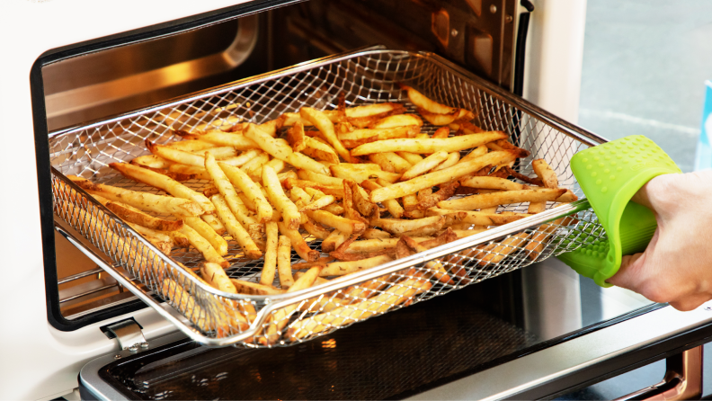 Person using a towel to pull out a wire rack covered in cooked french fries from an air fryer.