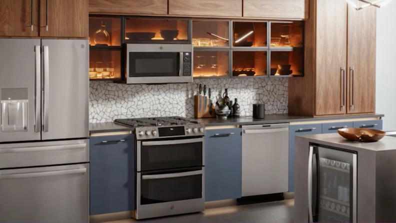 A kitchen fully equipped with GE appliances (from the left): a GE fridge, a GE range with a GE microwave above, a GE dishwasher and a knife set above it. On the right, there's a kitchen island with a GE wine fridge custom-installed inside.