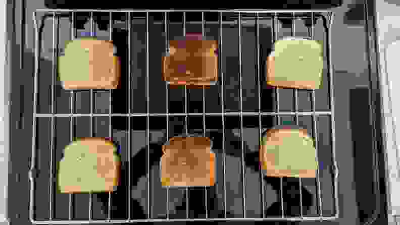 A rack from the electric range showing six slices of bread that were broiled; the middle two are quite burned.