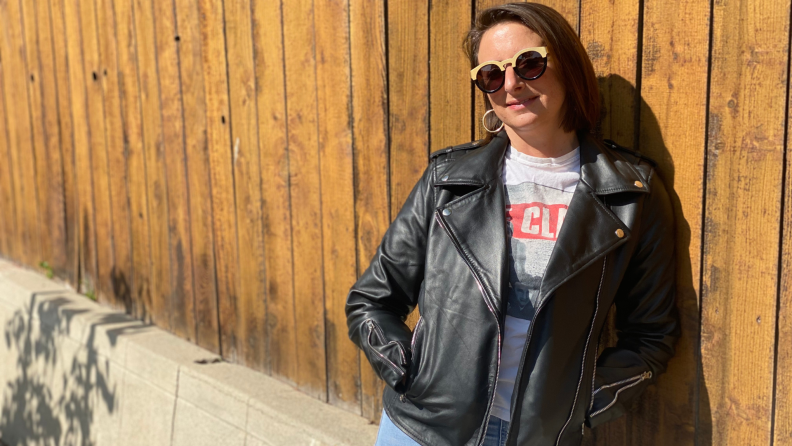 A woman stands against a fence in a black biker jacket