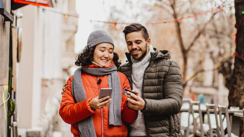 A man and woman looking at a cell phone on the street, laughing.