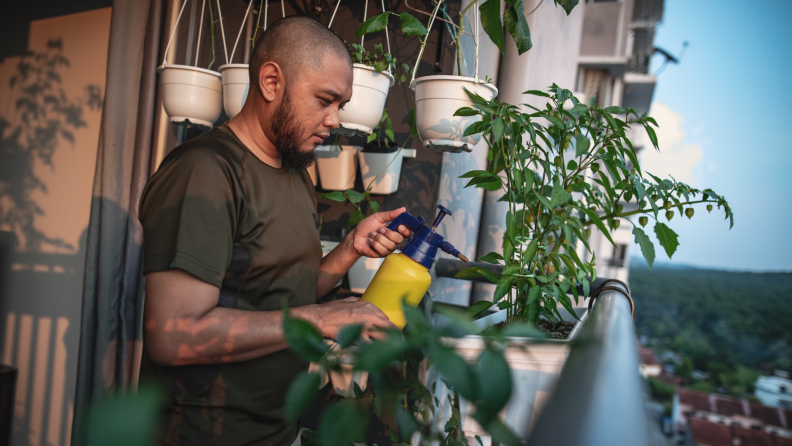 A person waters their home garden on a balcony.