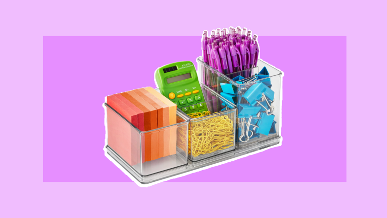 Clear acrylic desk organizer filled with multi-colored post-it notes, green calculator, purple clickable pens, yellow paperclips, and blue paper clamps.