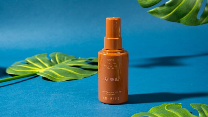 A bottle of face lotion against a blue background and foliage.