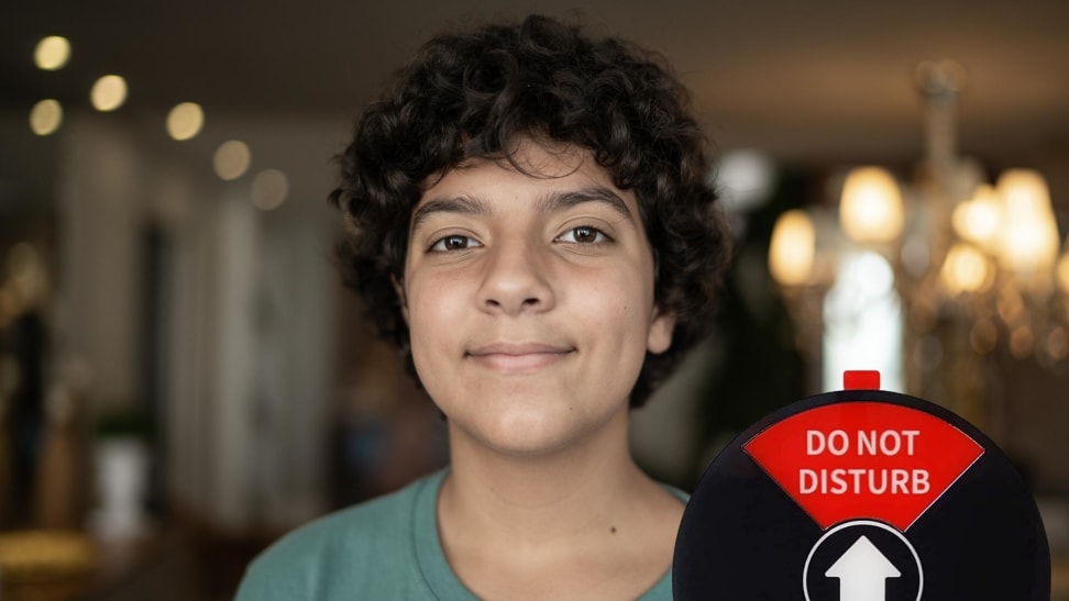 A young boy smiling at the camera. In the corner of the image is an round office privacy sign set to "Do Not Disturb"