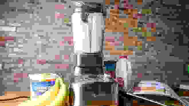 Blender with smoothie next to bananas, yogurt, and other smoothie materials