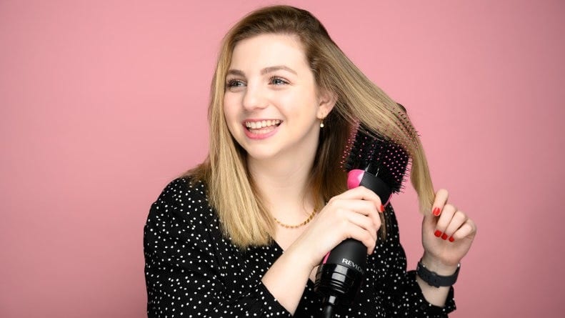 A person drys their hair with a handheld Revlon One Step brush.