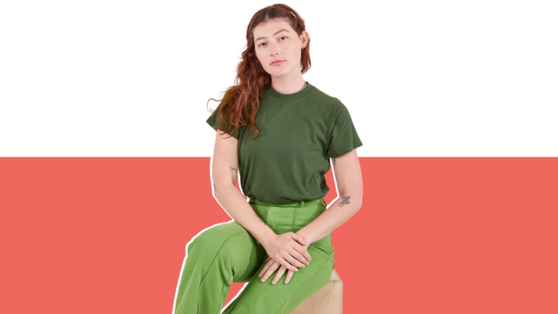 A woman in green shirt and pants sitting on a stool.