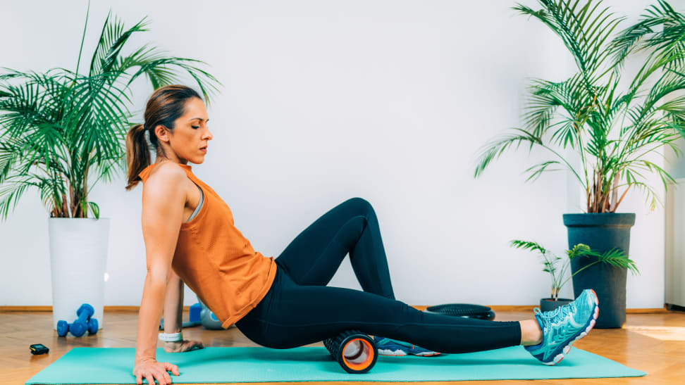 A woman using a foam roller to stretch her hamstring.