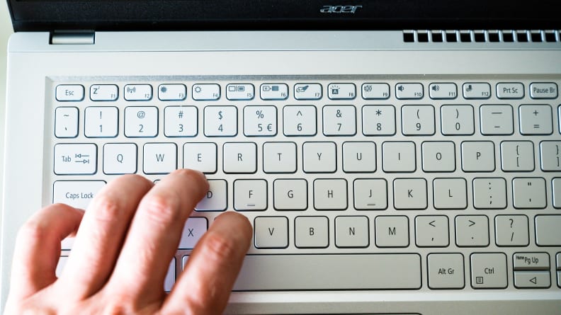A close up of a person's left fingers touching a silver laptop's keyboard.