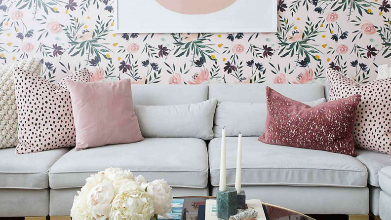 A couch with colorful wallpaper behind it and pink and white pillows on it