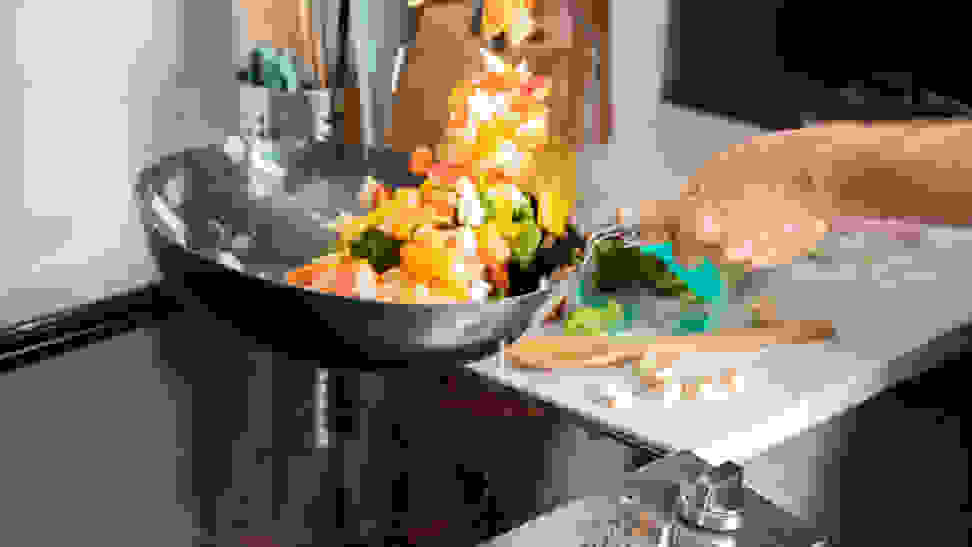A person is stir frying a medley of vegetables in a carbon steel wok over an electric cooktop.