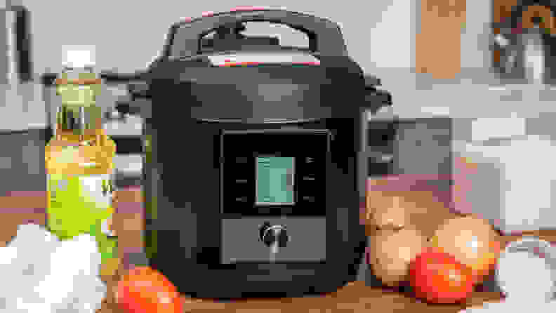 The Chef iQ pressure cooker sits on a white tiled counter accompanied by fresh produce on a cutting board.