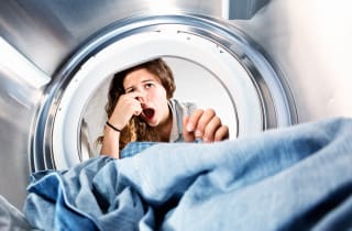 A woman leans into her washing machine and holds her nose