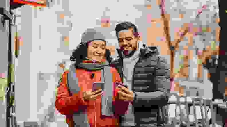 People smiling outdoors while making a purchase on smart phone.