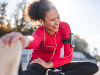 Woman stretching outside wearing headphones and workout clothes.