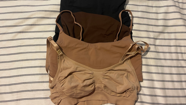 Four different shades of Skims bras, laid on a bed. The colors are tan, brown, dark brown, and black.