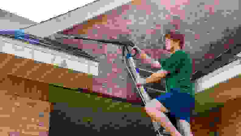 A homeowner climbs a ladder to power wash his home's brick exterior