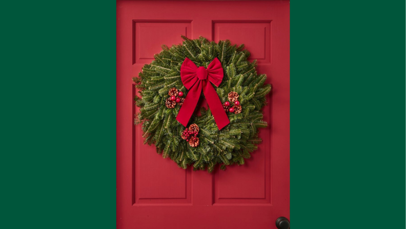 A classic fir wreath on a red door against a green background.