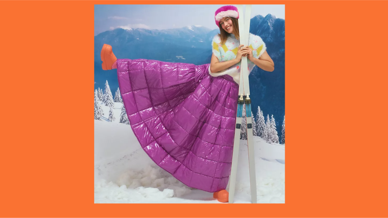 A model wearing a full-length purple maxi skirt and holding skiis.