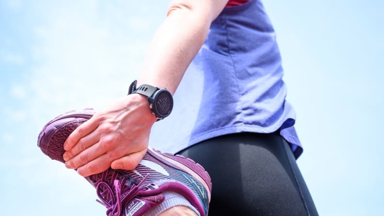 A woman stretching her quad wearing purple sneakers.