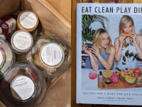 On left, individual plastic containers filled with food inside of paper bag . On right, front cover of _Eat Clean Play Dirty_ cookbook.