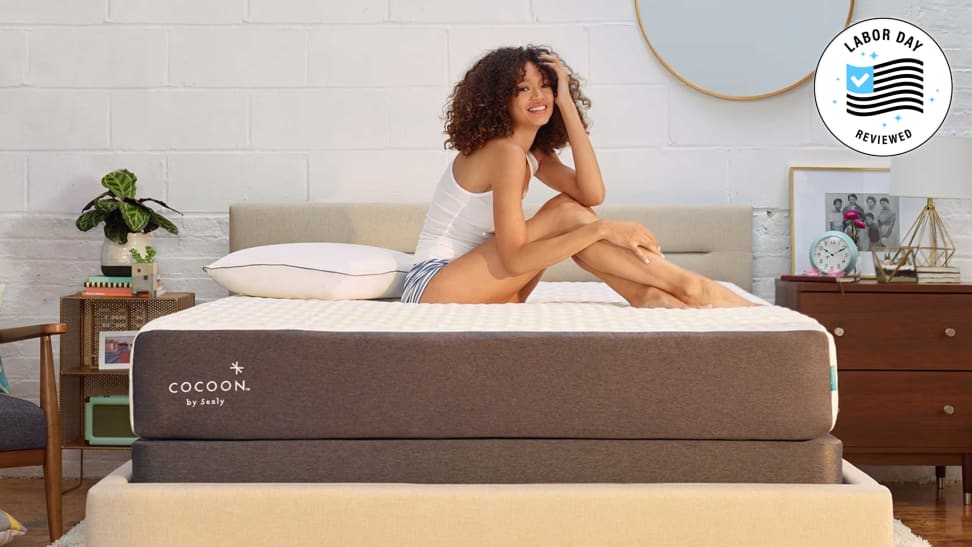 Cocoon by Sealy Chill mattress with woman on top of it and Reviewed Labor Day badge in a bedroom setup.