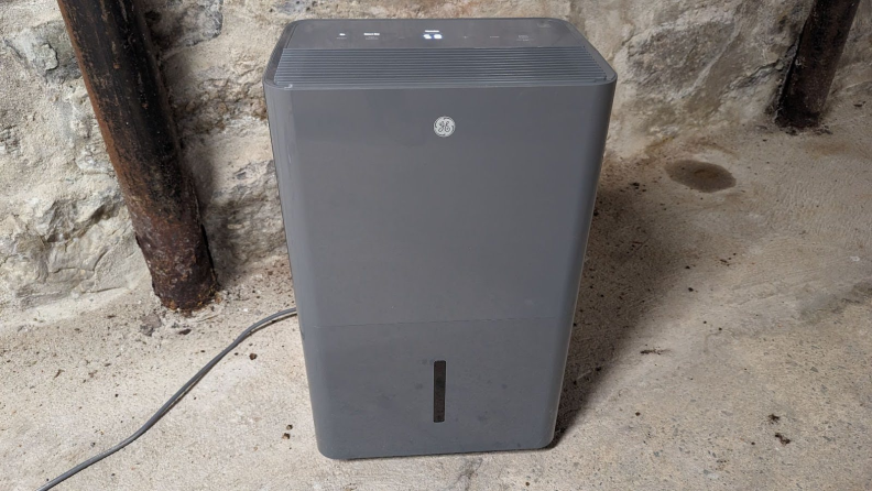 A gray GE AWYR50LC 50 pint smart dehumidifier located in a damp concrete basement.