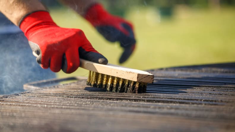 Hand scrubbing a gas grill with a brush.