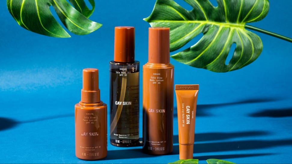 An assortment of tan Cay Skin bottles against a blue background and foliage.