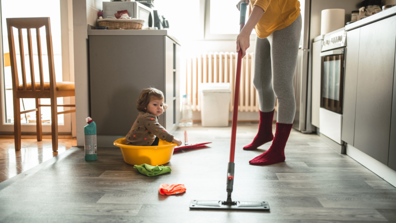 A person mopping the floors with a child seated on the floor.