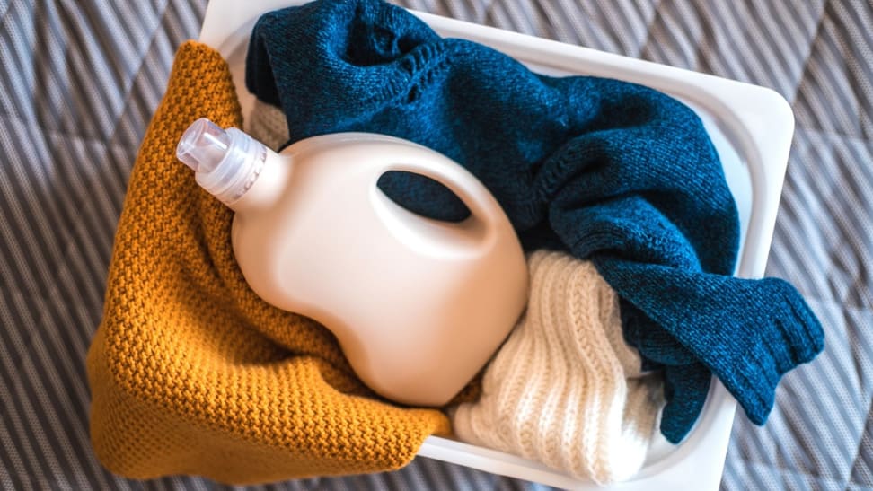 A bottle of laundry detergent and clothes in a hamper