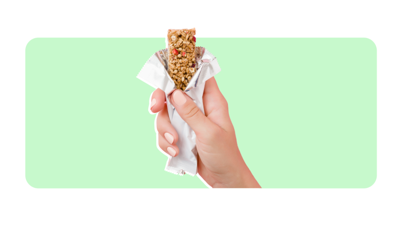 A person holding a food bar with a white wrapper on a green and white background.