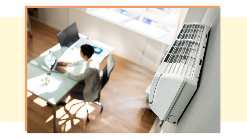 An image shot from above that shows a person sitting at a desk in a room working with an air conditioner on the wall.