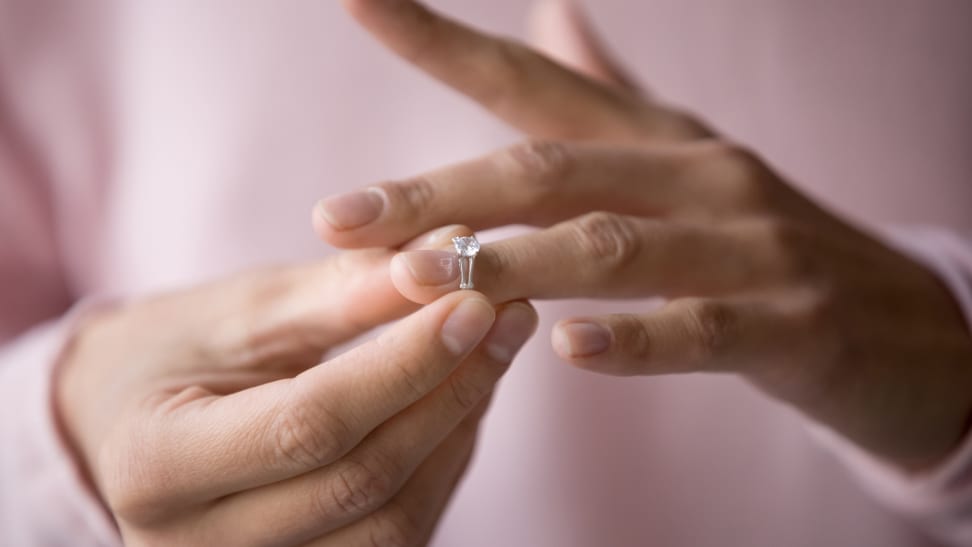 A close-up of a white person's hands, and removing a diamond engagement ring.