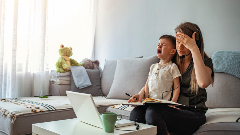 A screaming toddler sits on their parent’s lap while they work remotely.