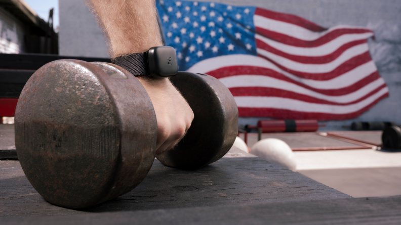 Person wearing fitness tracker band on wrist as she picks up dumbbell.