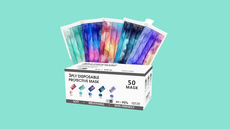 A 50-count box of X-CHENG disposable face masks with several masks in tie-dyed mixed colors of teal, purple, black, blue, pink, and yellow fanning out at the top.