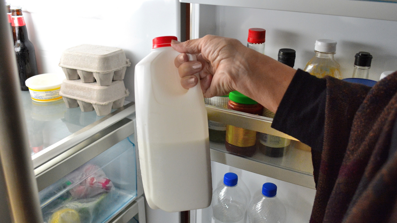 Person holding jug of milk in front of lit fridge with other food stored inside