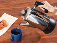 A person's hand pouring coffee from an electric coffee percolator into a blue mug