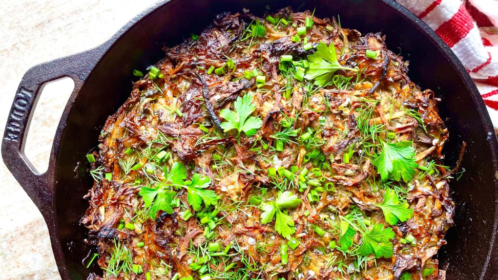 A close-up overhead photo of crispy potato kugel in a Lodge cast iron skillet, garnished with fresh parsley and dill.