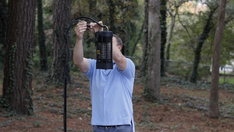 A man installs a bug zapper in the woods