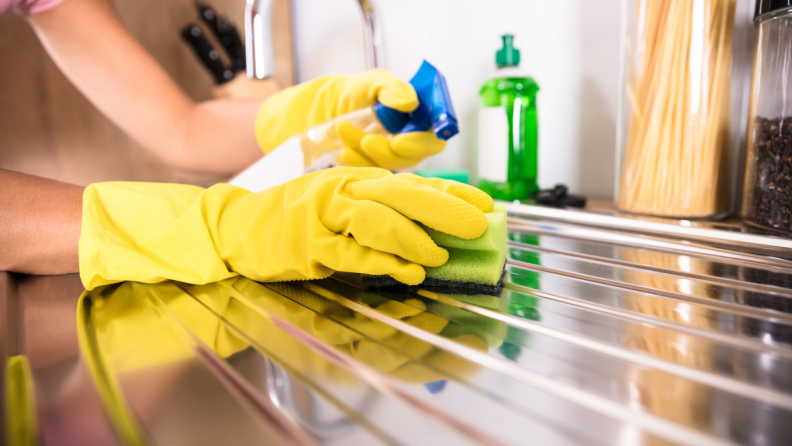 A gloved person wipes a stainless steel sink.