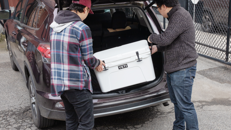 Two people putting a Yeti cooler in the back of a car.