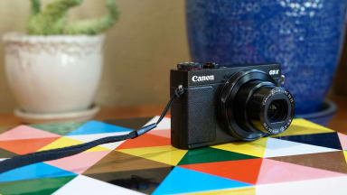 A black Canon point-and-shoot camera rests on a colorful tabletop.