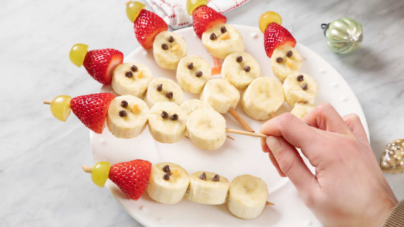 A hand pulling a snowman banana skewer off a plate