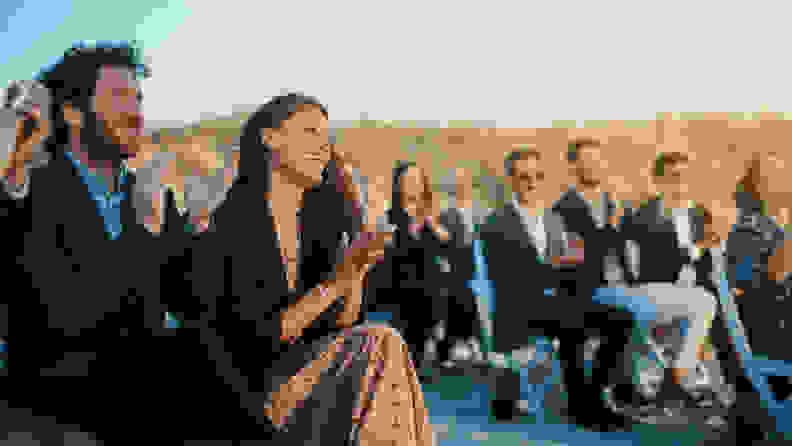 People sitting in chairs on a beach wearing suits and dresses.