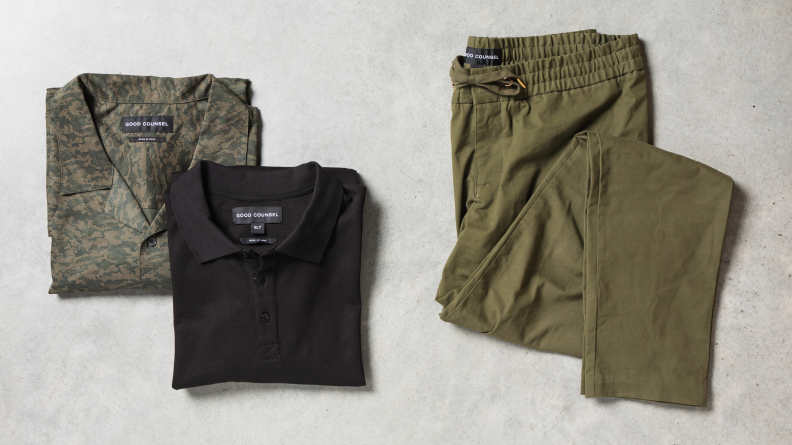 A camouflage-print shirt, black polo shirt, and green pants on a tabletop.